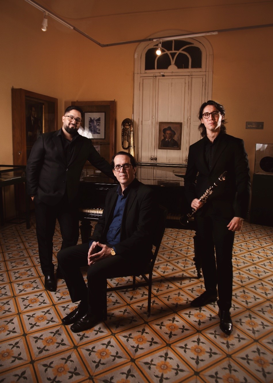 Photo of the trio: 2 musicians standing, a third musician seated in the center of the trio. (opens enlarged image)