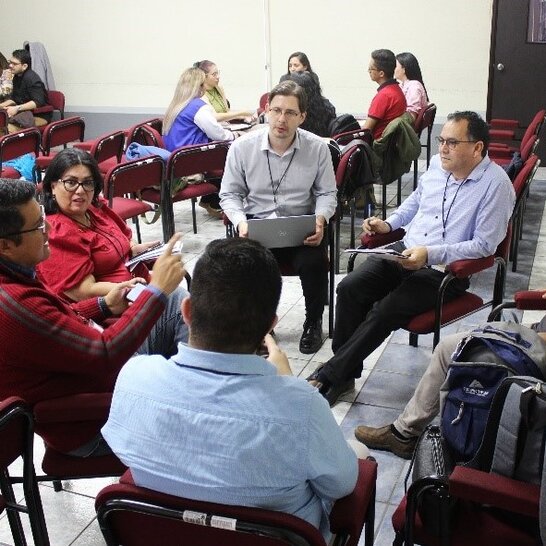 Cinco pessoas estão sentadas em círculo e conversam entre si. (abre uma ampliação da imagem)