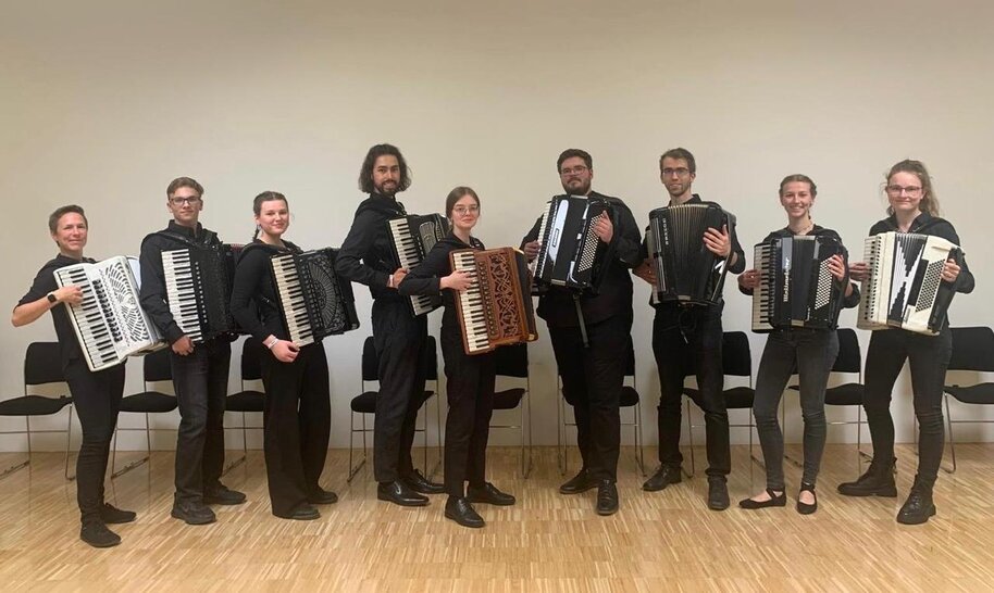 Foto der 9 Musikerinnen und Musiker des Ensembles im Stehen mit Akkordeons (öffnet Vergrößerung des Bildes)