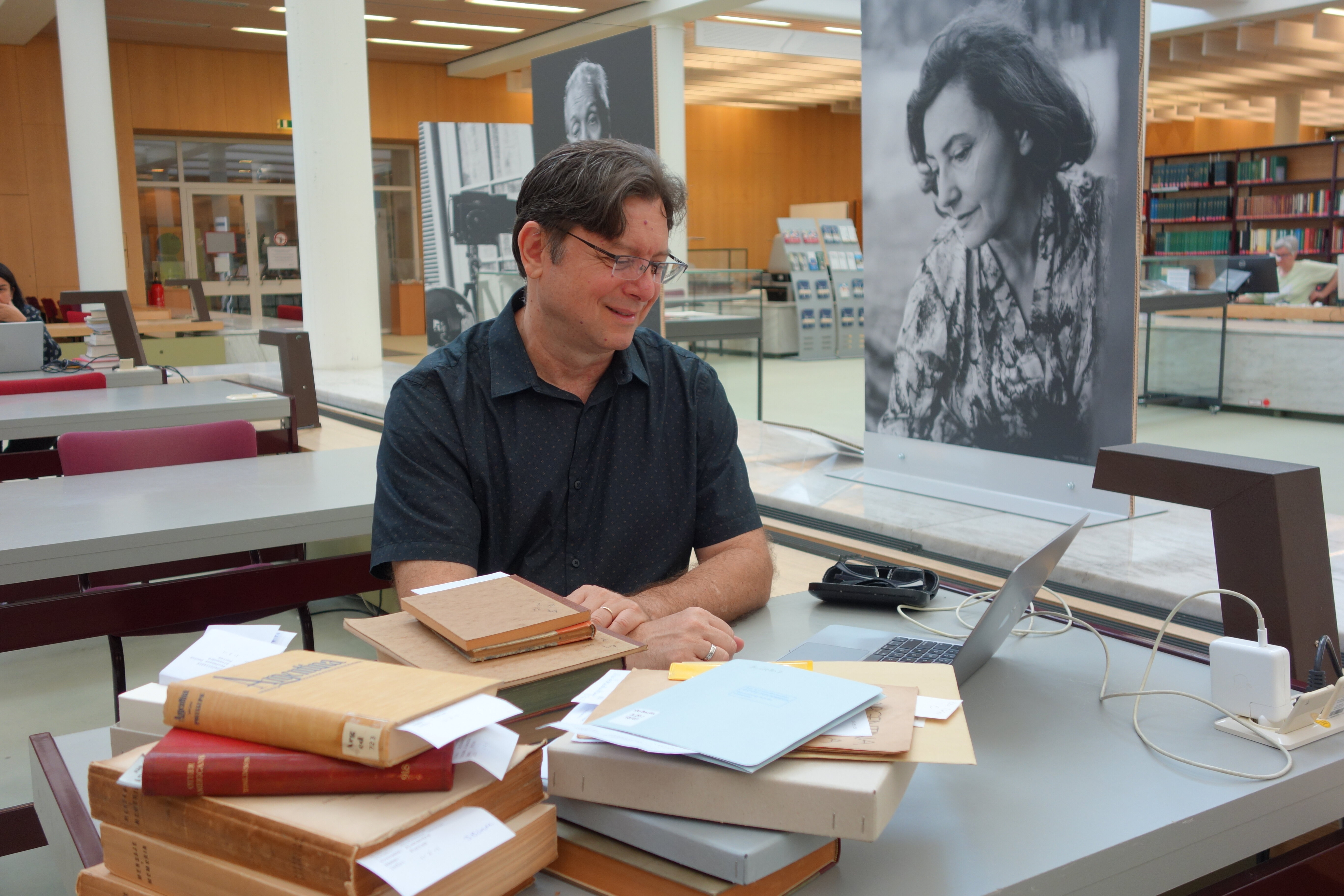 Pesquisador convidado Alexandre Fortes com livros e laptop em sua estação de trabalho na sala de leitura