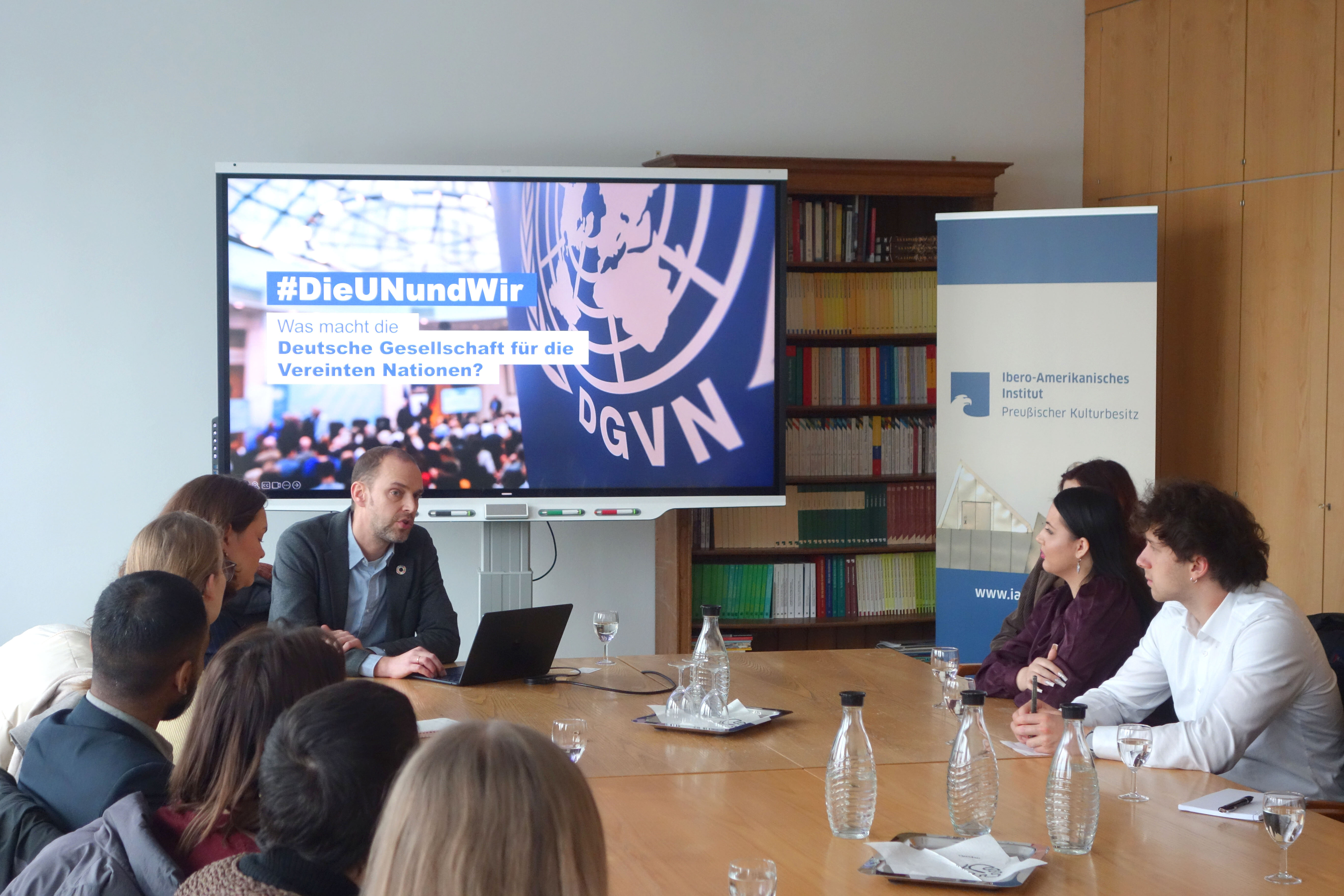 Um palestrante conversa com um grupo de estudantes em uma grande mesa de reuniões