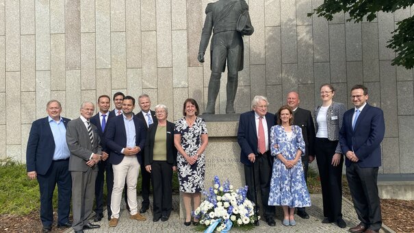 Personen und ein Blumenkranz vor einer Bronzestatue