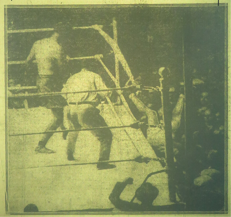 Historical photo of a boxing match while one of the boxers is being thrown out of the ring