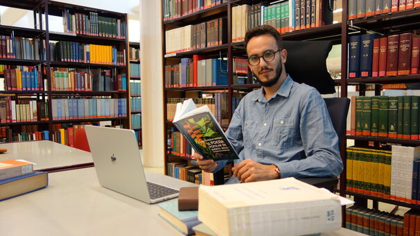Gastwissenschaftler Ewerton Barros mit Büchern an seinem Arbeitsplatz im Lesesaal
