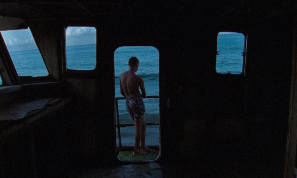 Un joven mira al agua desde la ventana de un barco.