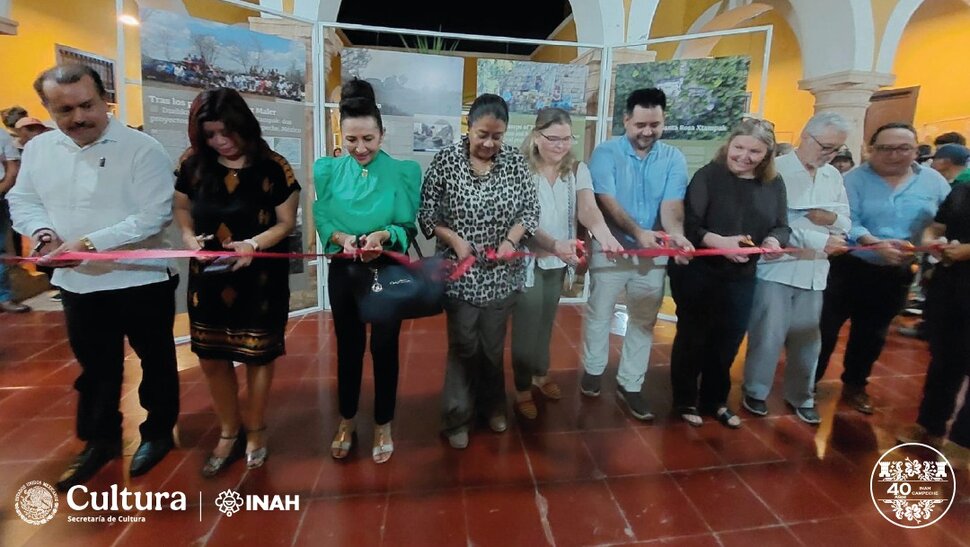 9 Personen zerschneiden ein rotes Band vor ihnen, im Hintergrund Ausstellungstafeln