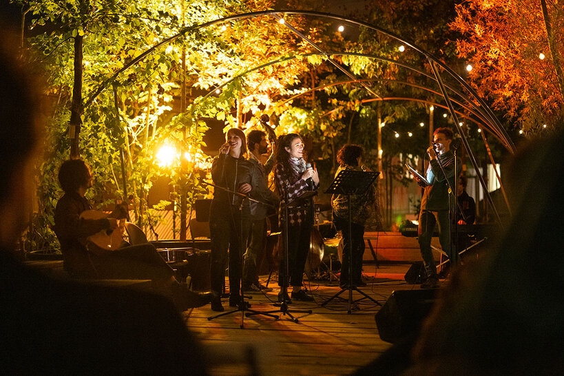 Drei Musikerinnen und Musiker auf einer Open-Air-Bühne, begleitet von einer Gitarre.