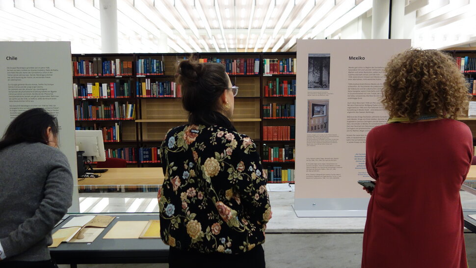 Mehrere Personen schauen sich Tafeln und Vitrinen in der Ausstellung an (abre uma ampliação da imagem)