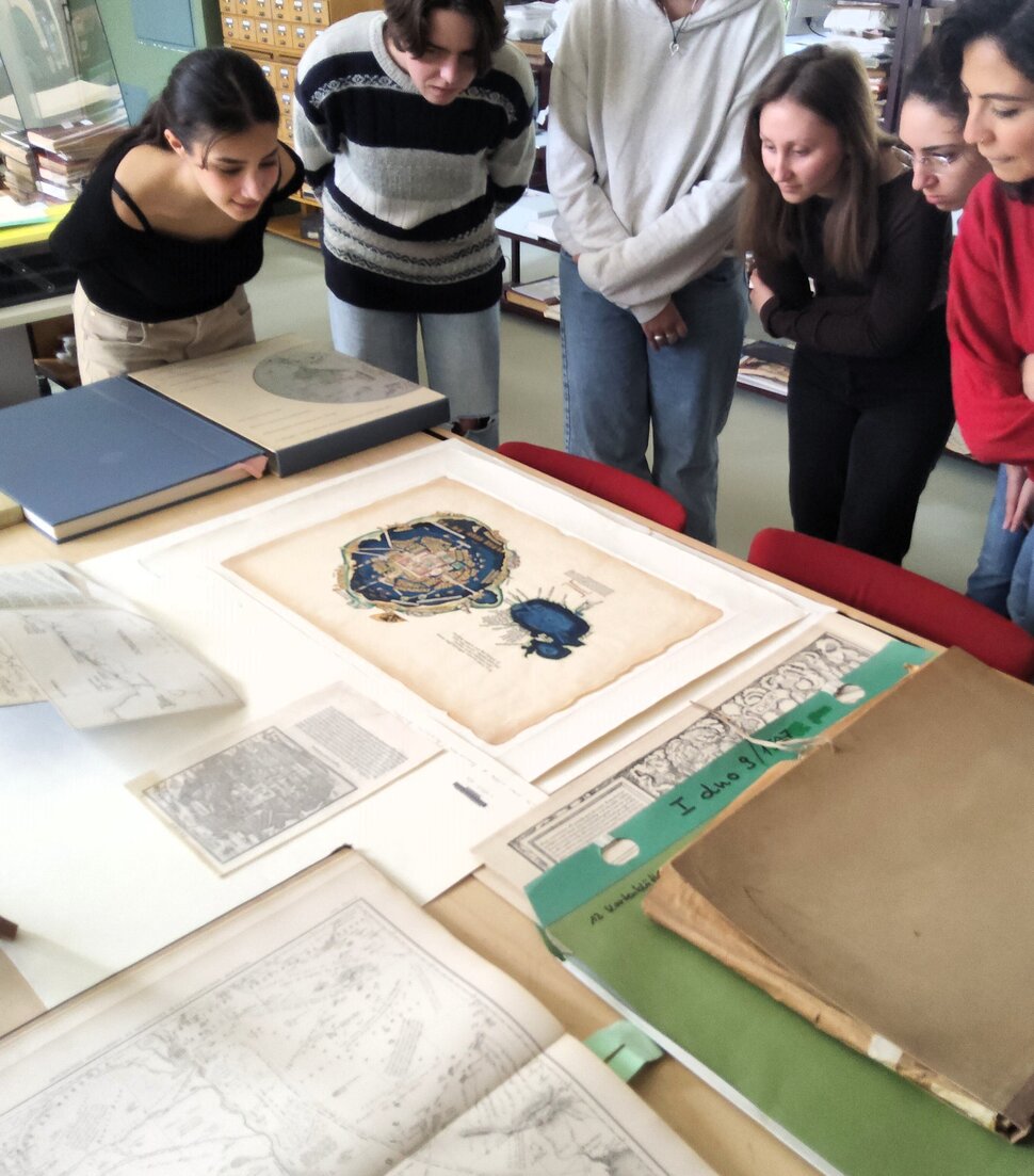 Un grupo de estudiantes observa una selección de mapas históricos en la sala de lectura de mapas.