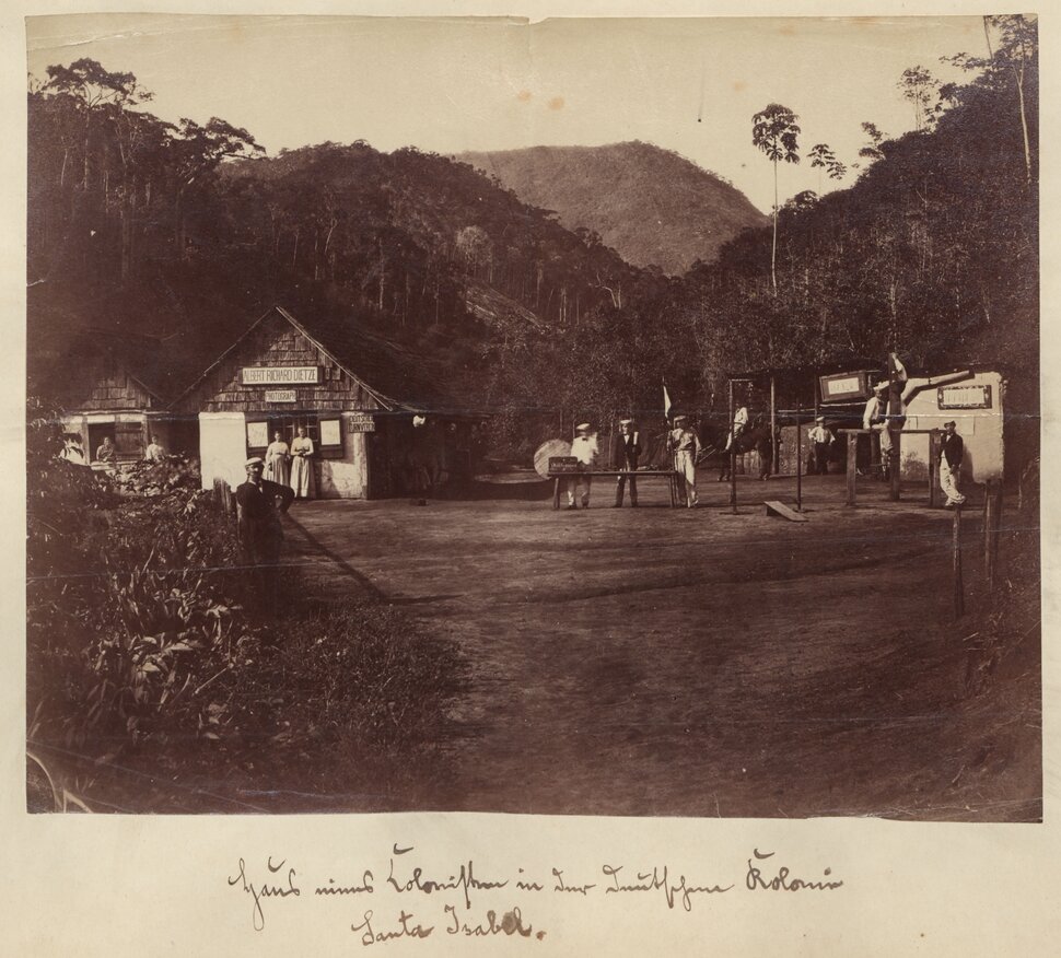 Historisches Foto mit drei Personen auf unbefestigter Straße, links und rechts Gebäude